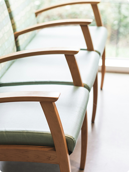 Three light green cushioned chairs with wooden armrests are arranged in a row near a large window.