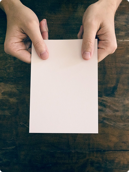 Two hands holding a blank white sheet of paper over a wooden surface.